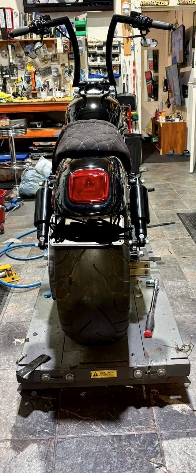Wide rear tyre and tail light of a Harley, viewed from behind on the lift