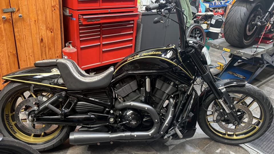 Black Harley-Davidson V-Rod with gold pinstriping and gold wheels, side on, in the workshop